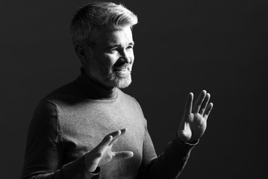 Photo of Portrait of smiling man gesturing on dark background. Black and white effect