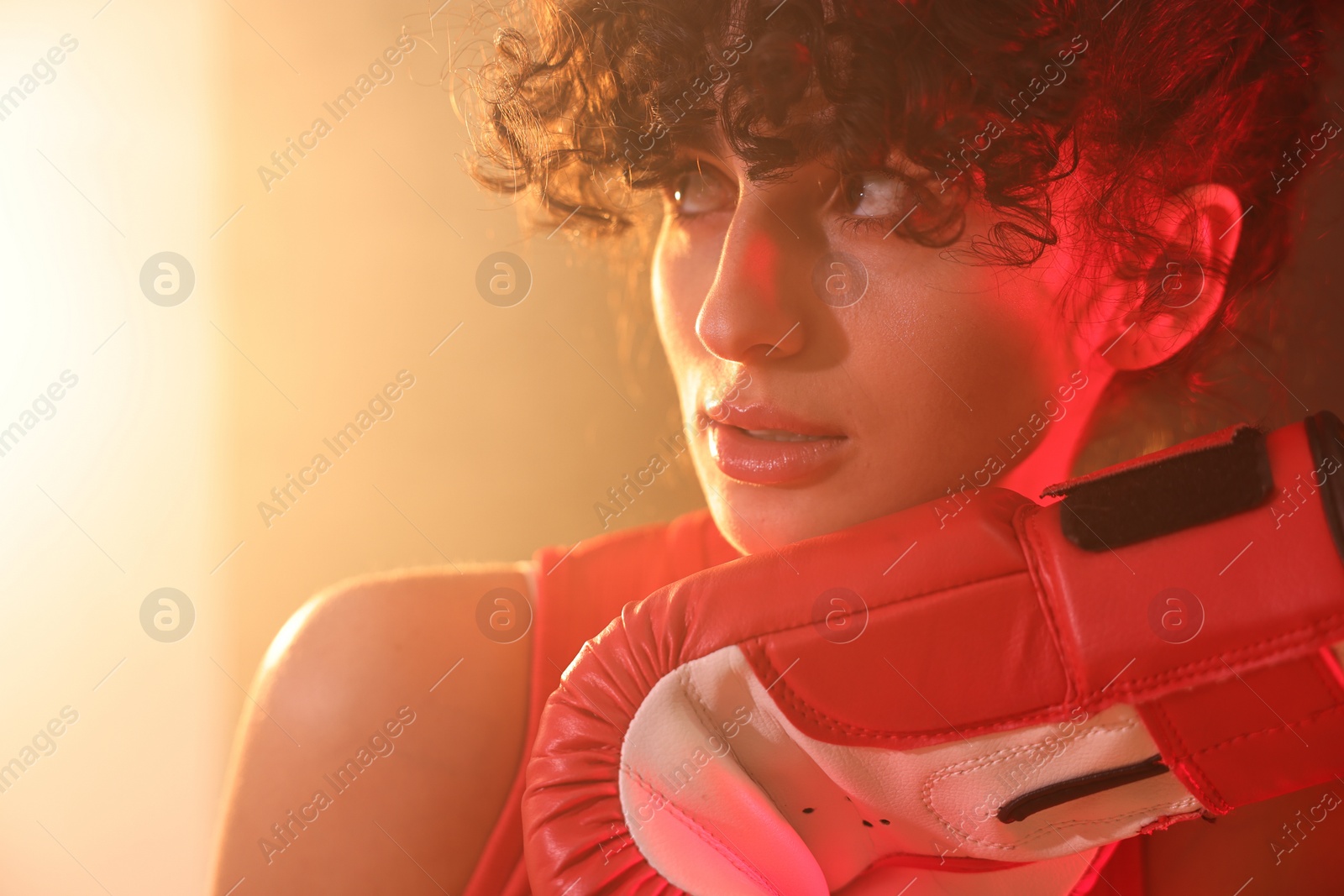 Photo of Beautiful young woman with boxing gloves on color background in neon lights and smoke, closeup