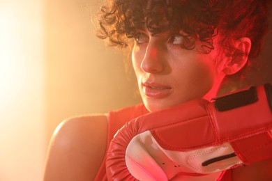 Beautiful young woman with boxing gloves on color background in neon lights and smoke, closeup