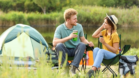 Photo of Young couple with hot drinks resting outdoors. Camping vacation