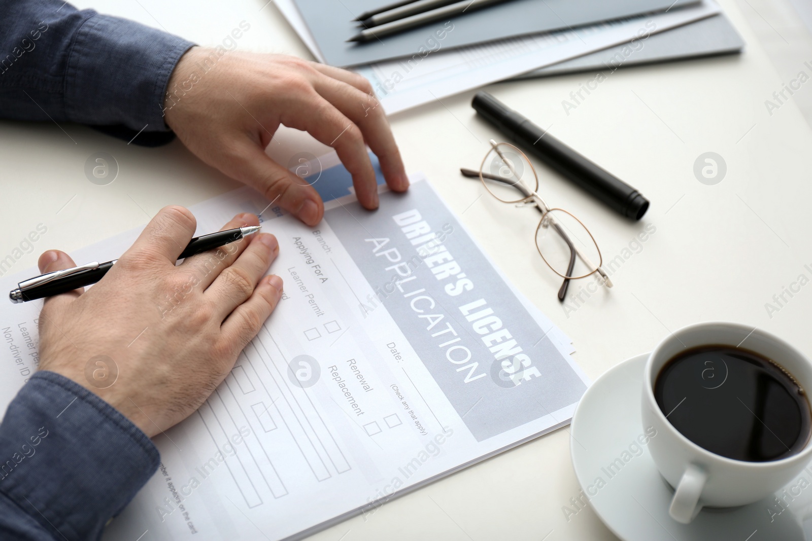 Photo of Man filling in driver's license application form at white table, closeup