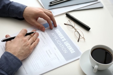 Man filling in driver's license application form at white table, closeup