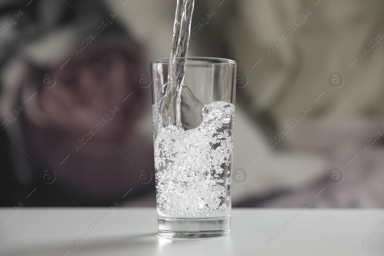 Photo of Pouring water into glass on table against blurred background