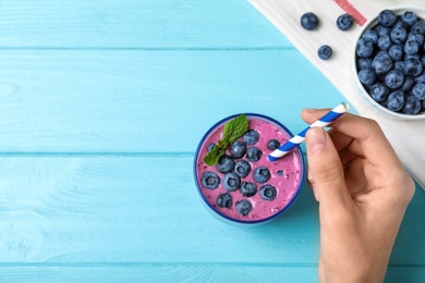 Photo of Young woman with glass of blueberry smoothie at light blue wooden table, top view. Space for text