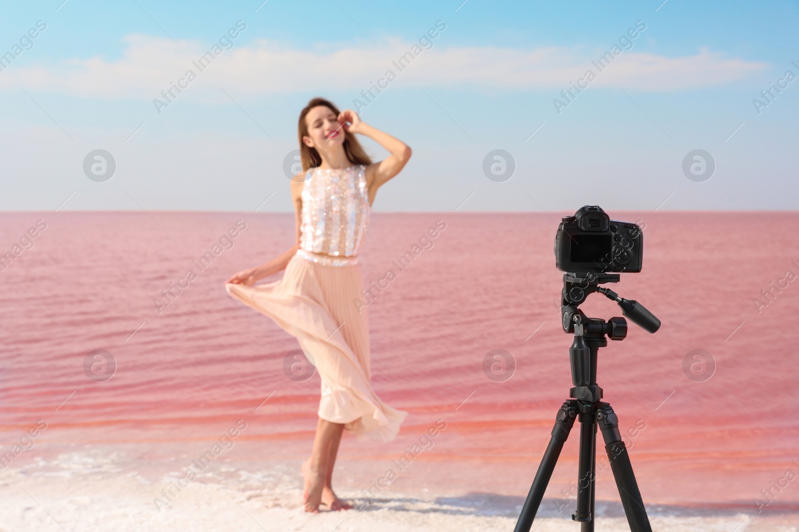 Photo of Young woman posing in front of professional camera near pink lake on sunny day