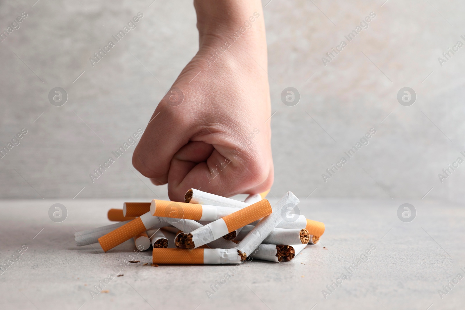 Photo of Stop smoking. Woman crushing cigarettes at grey table, closeup