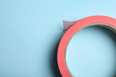 Photo of Roll of pink adhesive tape on light blue background, top view. Space for text