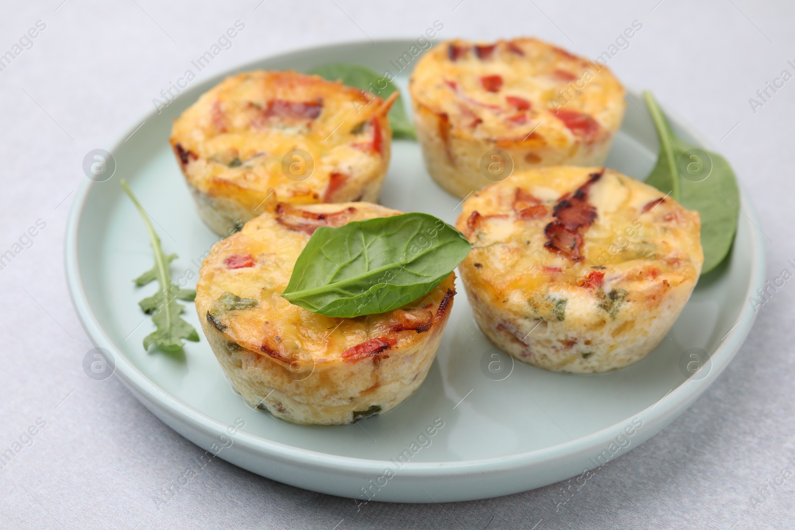 Photo of Freshly baked bacon and egg muffins with cheese on light gray table, closeup