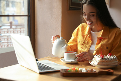 Photo of Young blogger pouring tea into cup at table in cafe