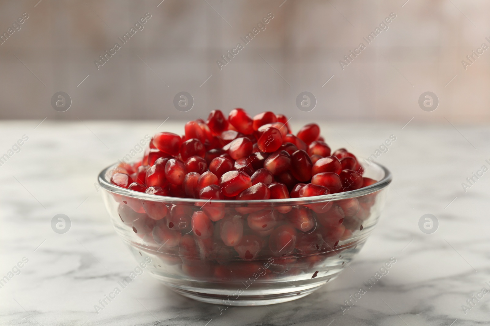Photo of Ripe juicy pomegranate grains in bowl on white marble table, closeup