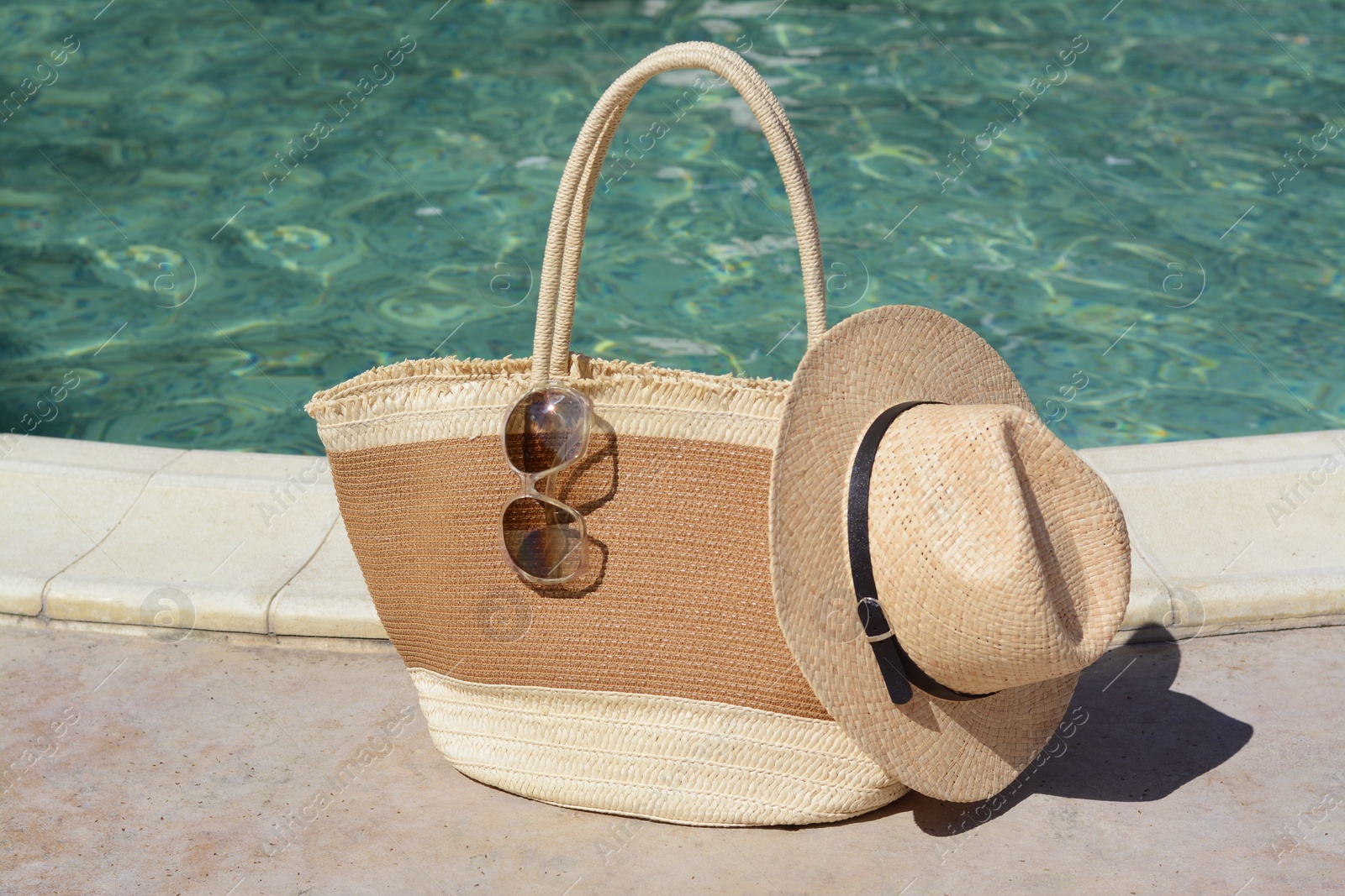 Photo of Stylish bag, sunglasses and hat near outdoor swimming pool on sunny day. Beach accessories