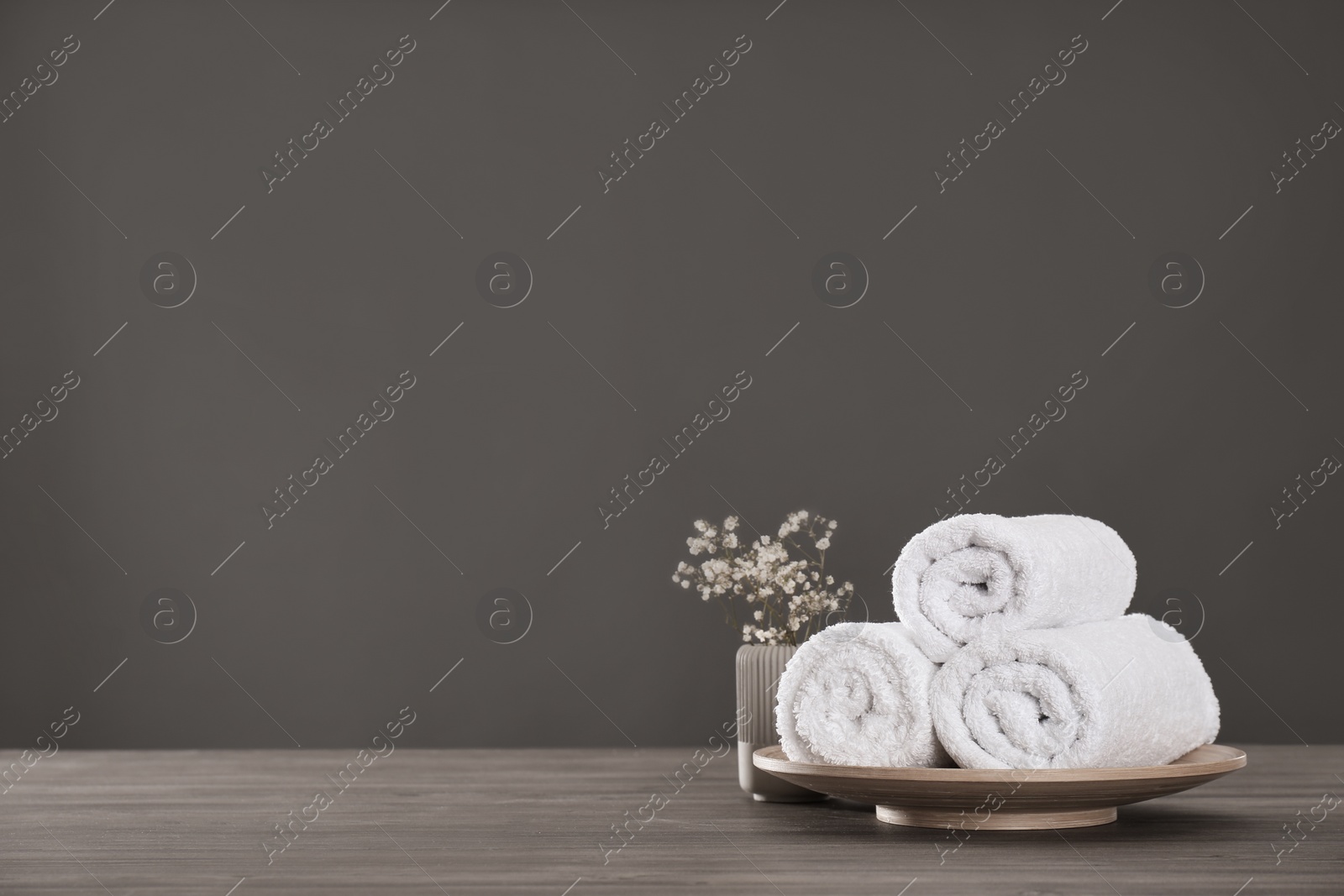Photo of Fresh rolled towels and plant on grey wooden table. Space for text