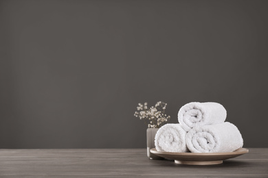 Photo of Fresh rolled towels and plant on grey wooden table. Space for text