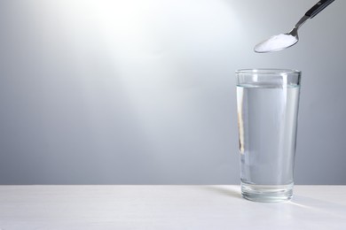 Photo of Spoon with baking soda over glass of water on white table against light grey background. Space for text