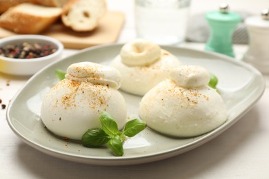 Photo of Delicious burrata cheese with basil on white wooden table, closeup