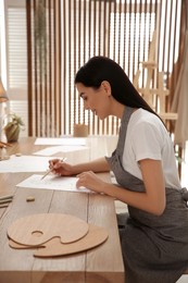 Young woman drawing with pencil at table indoors