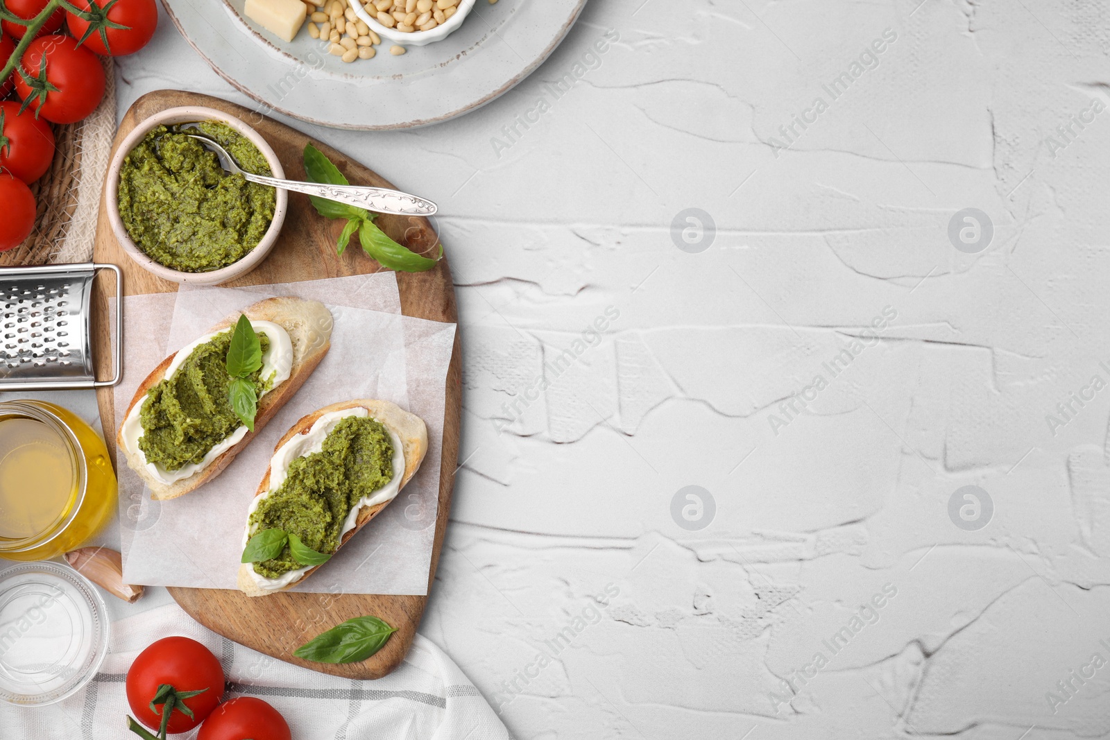 Photo of Tasty bruschettas with pesto sauce and ingredients on white textured table, flat lay. Space for text