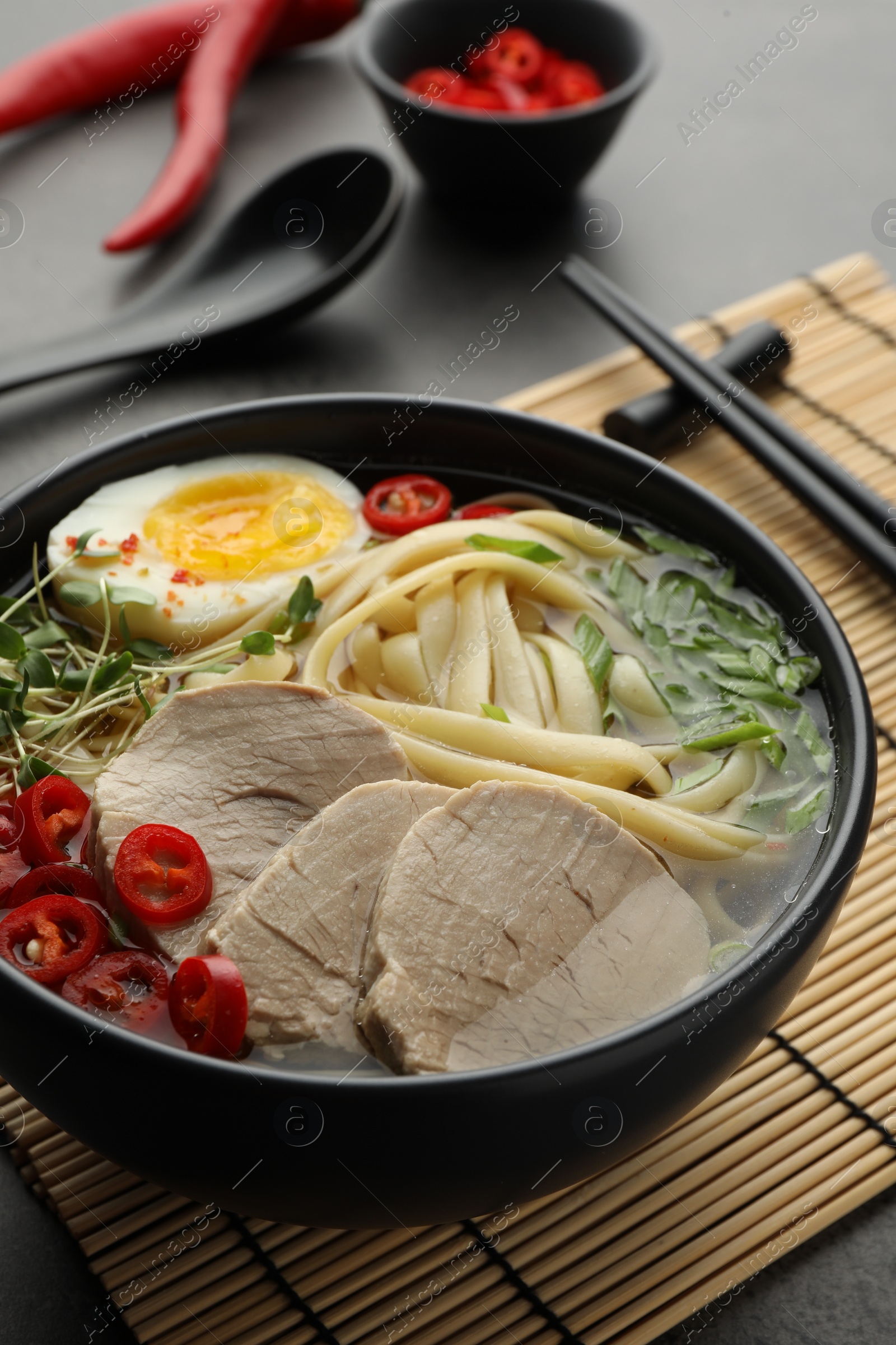 Photo of Delicious ramen with meat in bowl served on grey table, closeup. Noodle soup