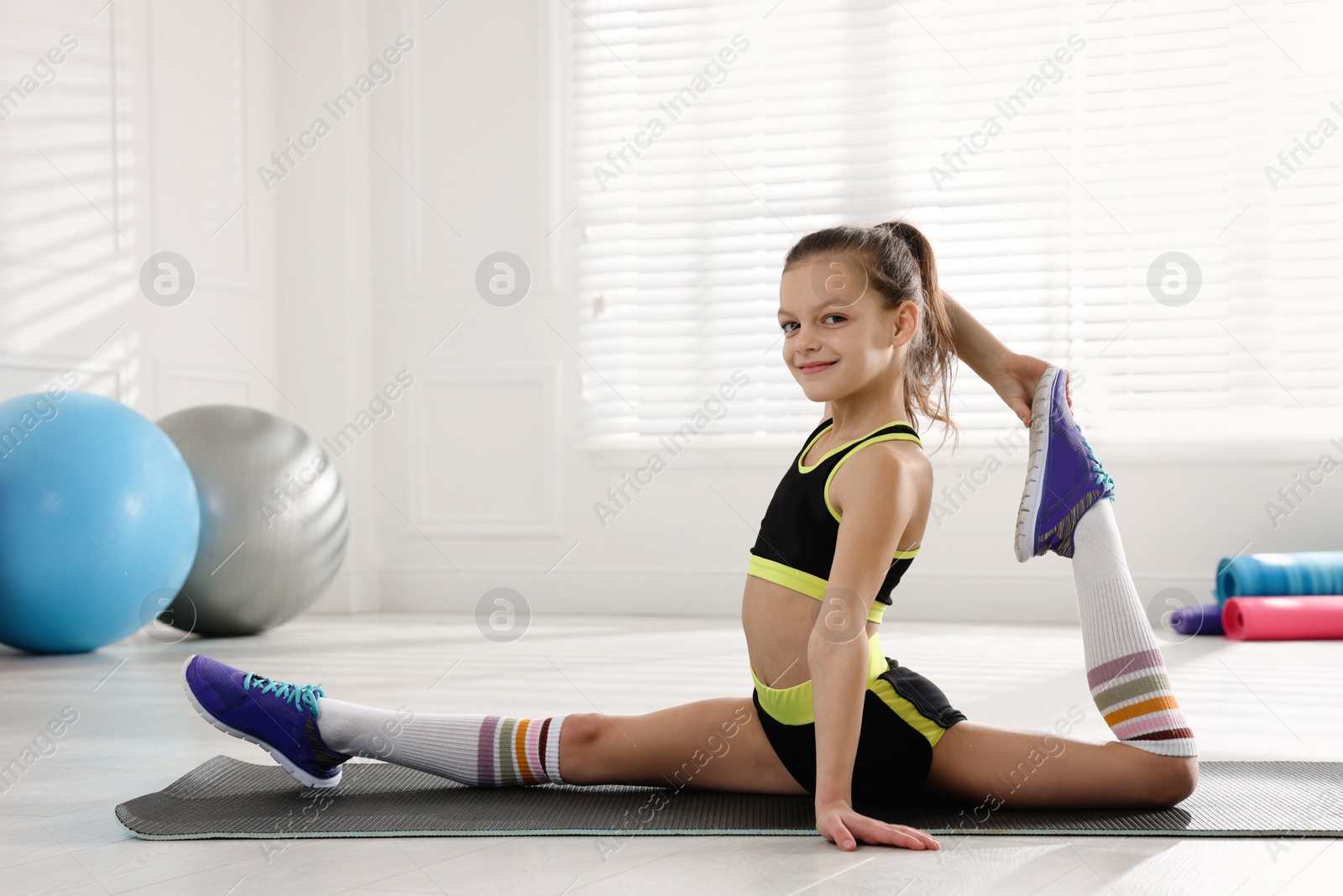 Photo of Cute little girl doing gymnastic exercise indoors
