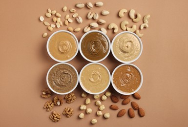 Many tasty nut butters in bowls and nuts on beige table, flat lay