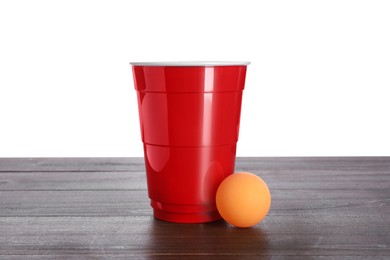 Photo of Plastic cup and ball for beer pong on wooden table against white background