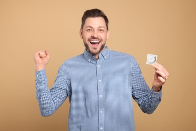 Photo of Excited man holding condom on beige background