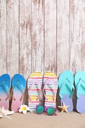 Different bright flip flops and sunglasses on sand near wooden wall, space for text. Summer beach accessories