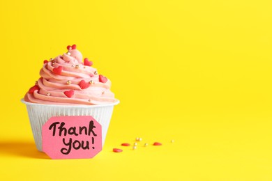 Photo of Tasty cupcake and note with phrase Thank You on yellow background, space for text
