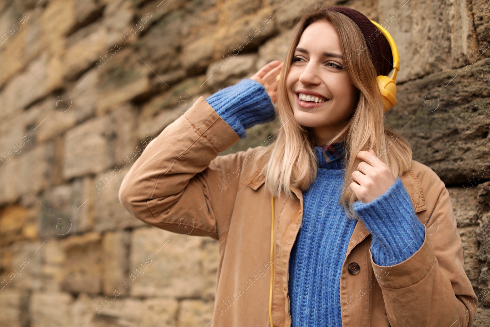 Photo of Young woman with headphones listening to music near stone wall. Space for text