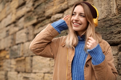 Young woman with headphones listening to music near stone wall. Space for text