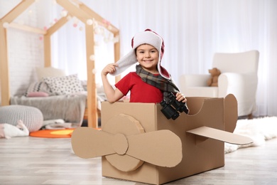 Cute little boy playing with binoculars and cardboard airplane in bedroom