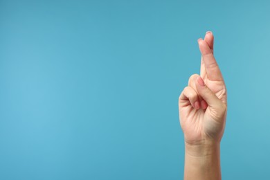 Photo of Woman crossing her fingers on light blue background, closeup. Space for text