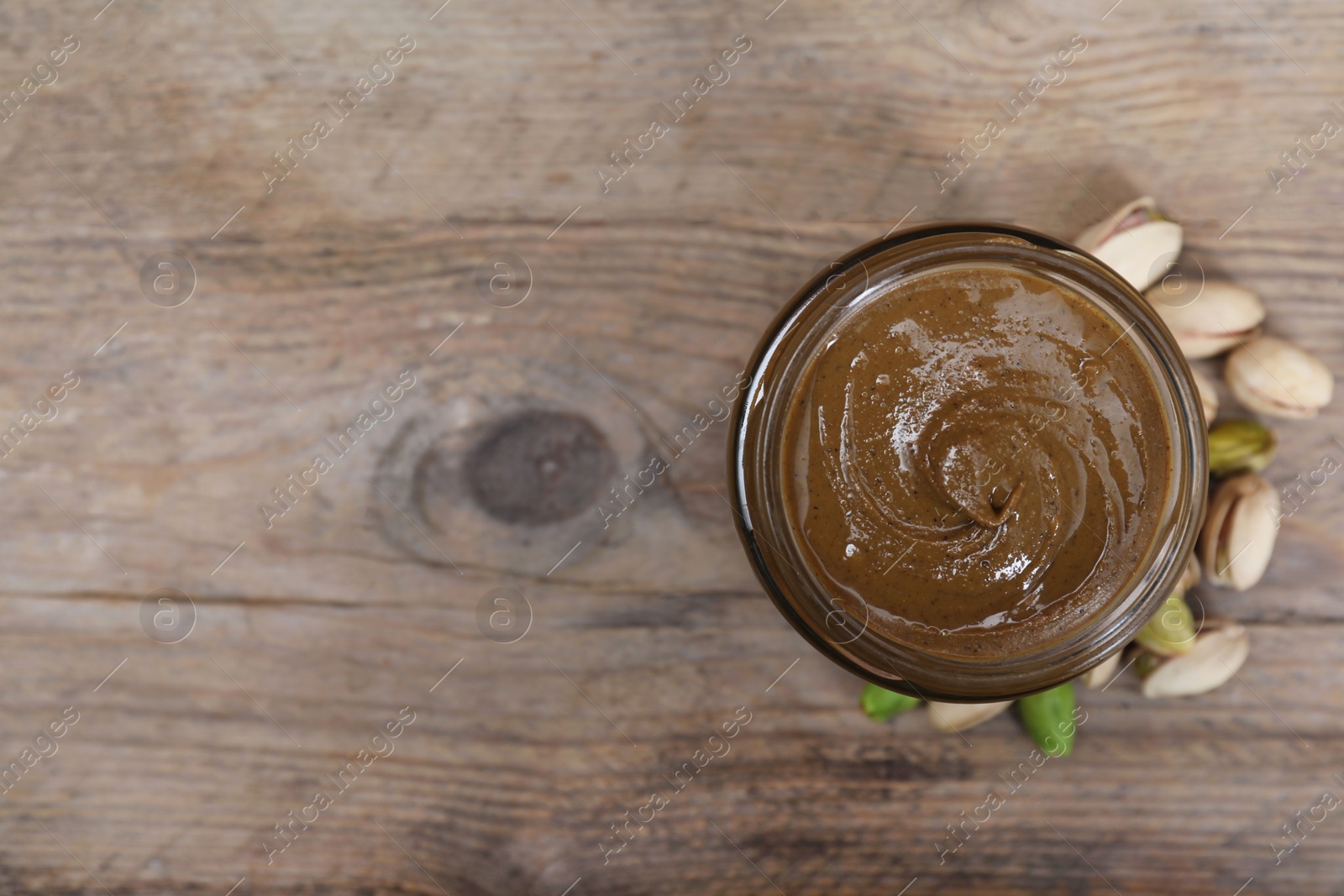 Photo of Tasty pistachio nut paste in jar on wooden table, top view. Space for text