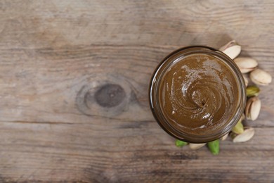 Tasty pistachio nut paste in jar on wooden table, top view. Space for text