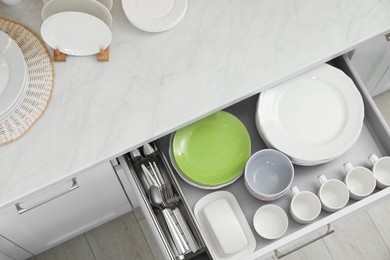 Clean plates, bowls, cutlery and cups in drawer indoors, top view