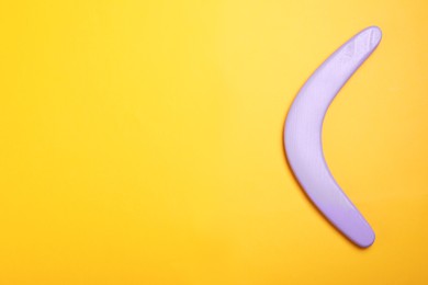 Photo of Lilac boomerang on yellow background, top view. Space for text