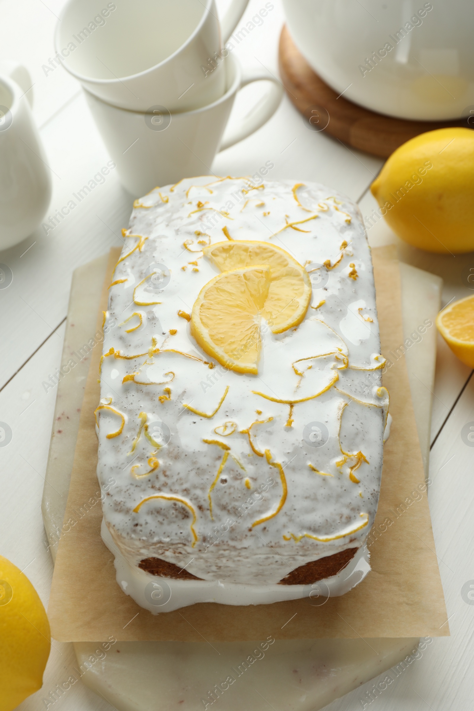 Photo of Tasty lemon cake with glaze and citrus fruits on white table, closeup