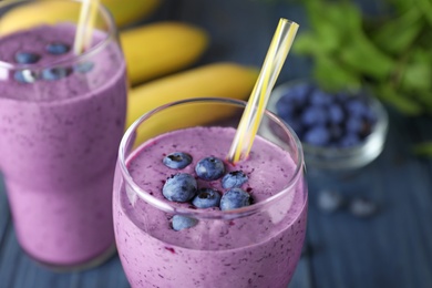 Glasses of delicious blueberry smoothie on blue wooden table