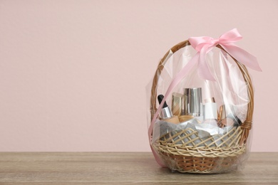 Photo of Wicker gift basket with cosmetic products on wooden table. Space for text