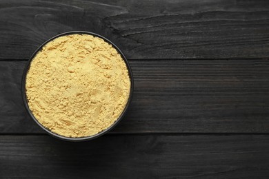 Photo of Bowl of aromatic mustard powder on black wooden table, top view. Space for text