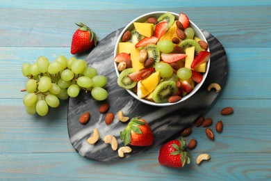 Photo of Tasty fruit salad in bowl and ingredients on light blue wooden table, flat lay