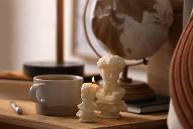 Beautiful David bust candles and cup of hot drink on table indoors, space for text