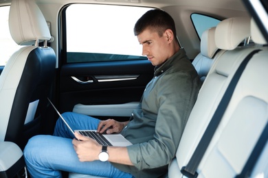 Attractive young man working with laptop on backseat in luxury car