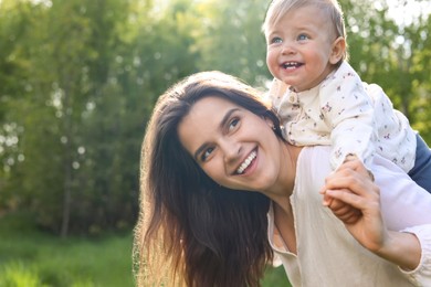 Happy mother playing with her cute baby in park on sunny day, space for text