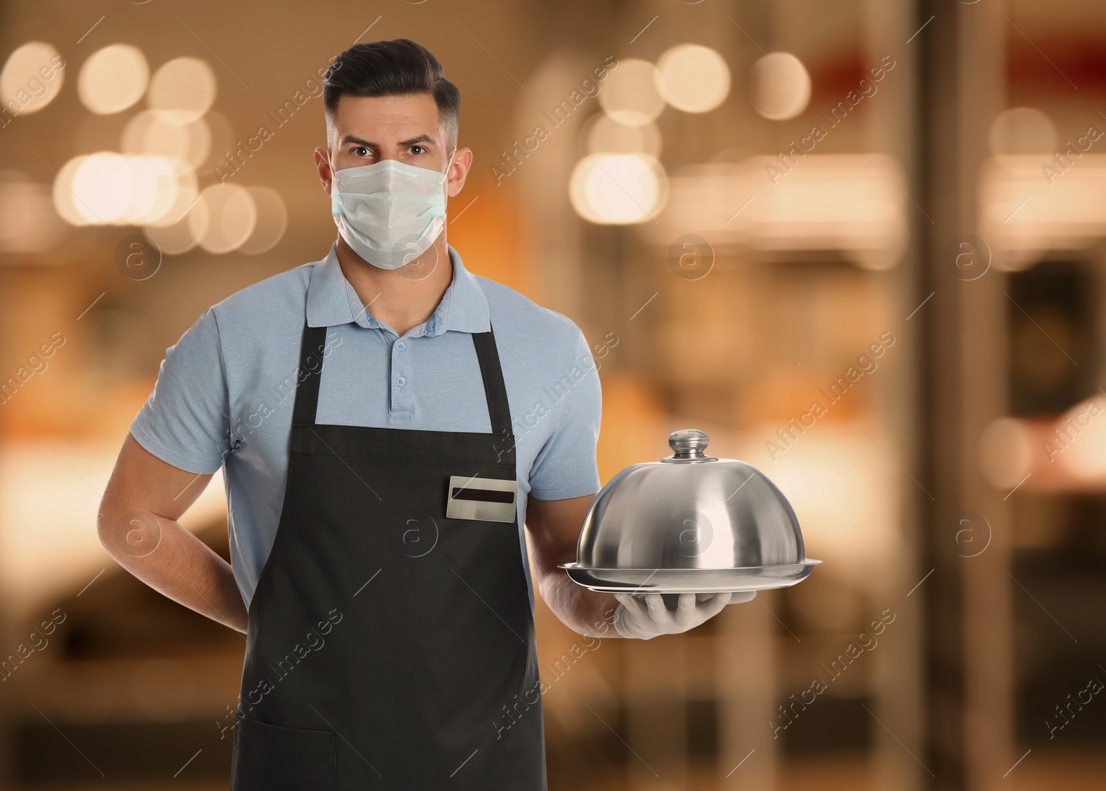Image of Waiter in medical face mask holding tray with lid in restaurant