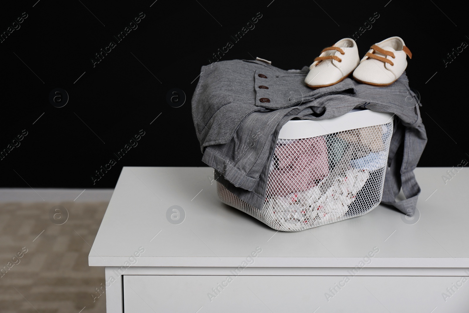 Photo of Laundry basket with baby clothes and shoes on white table indoors, space for text