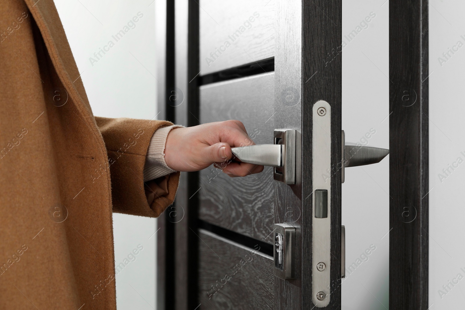 Photo of Woman opening wooden door indoors, closeup of hand on handle