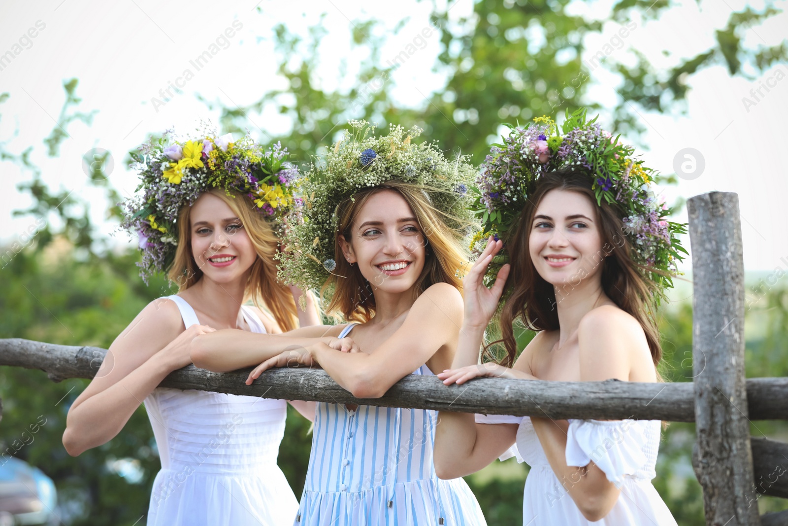 Photo of Young women wearing wreaths made of beautiful flowers near wooden fence