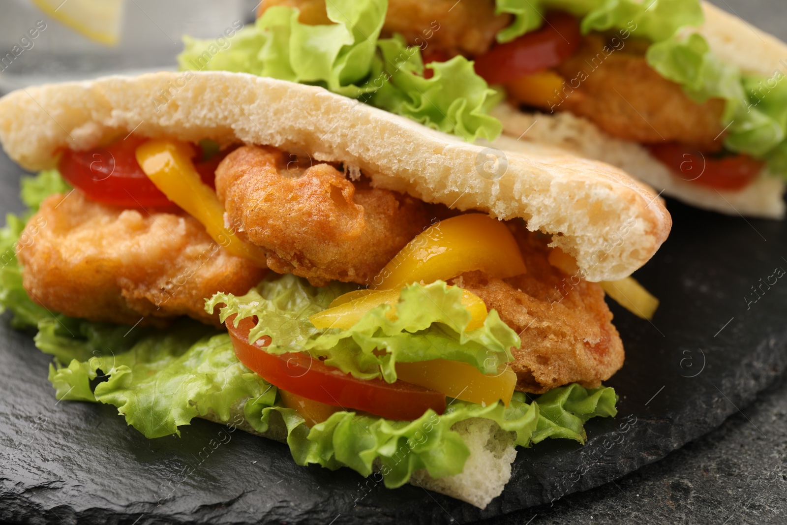 Photo of Delicious pita sandwiches with fried fish, pepper, tomatoes and lettuce on dark grey table, closeup