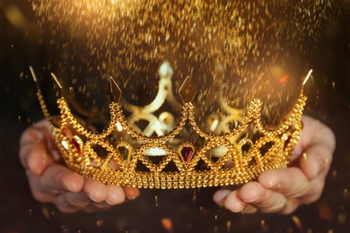 Image of Fantasy world. Woman holding beautiful golden crown lit by magic light, closeup
